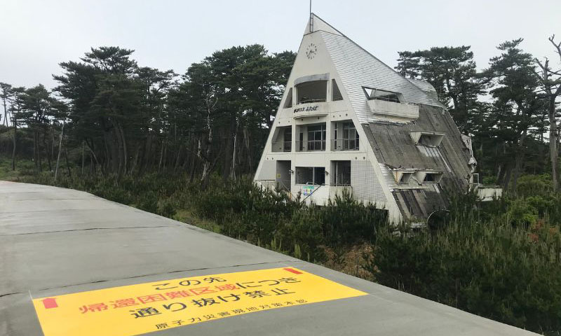 雙葉町海堤旁被海嘯摧殘過破敗的房子，海堤地面上寫著返還困難的界線。（圖/鍾令和）