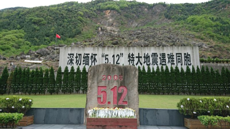 北川老縣城地震遺址紀念碑,碑後山坡的石堆掩蓋了北川中學,校園只剩下一根旗桿,罹難者至今仍在亂石堆下。