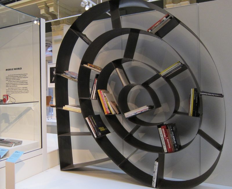 Ron Arad 的《This Mortal Coil》螺旋書架以鋼帶構成主體，透過長短不一的模組化分隔件撐開層板，兩端採鉸接設計，一端鉚接、一端螺栓連結，可調整、可拆卸、可重組。具高度模組性與可變形結構，展現產品生命周期管理與永續設計理念。（圖／ 謝玉鈴）