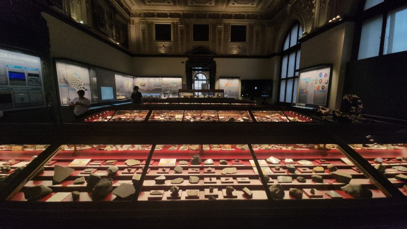 維也納自然史博物館隕石廳的全景，中央長形展櫃系統性地展示各類隕石。陳列有序的展櫃，每一顆隕石都擁有自己的身分證（標籤），詳細記錄其名稱、分類、發現／墜落地點和日期。（圖／陳君榮）