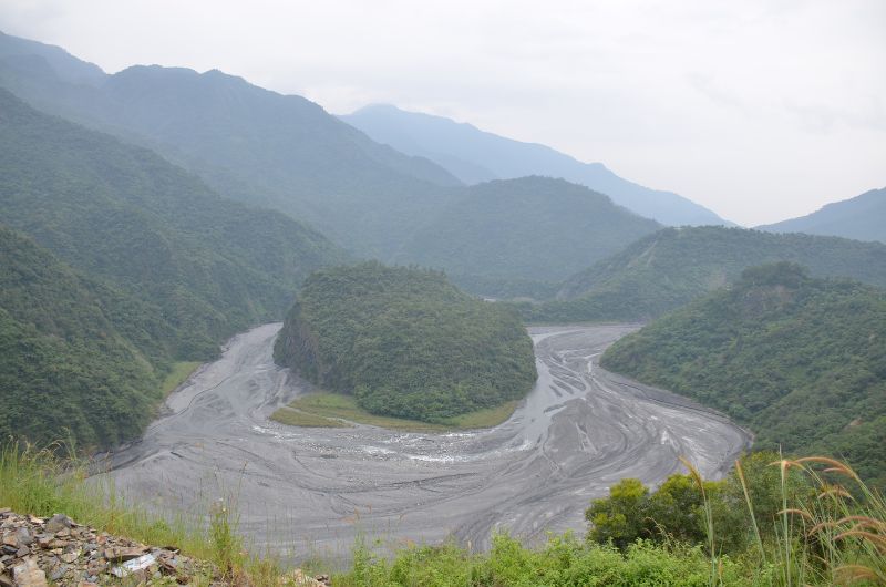高雄市茂林區蛇頭山的成育曲流，在河流側蝕作用下，凹岸處坡度變陡（圖下方）。凸岸處亂流作用較弱，易發生堆積作用，坡度變緩（圖中央的蛇頭）。形成此兩岸不對稱的成育曲流。